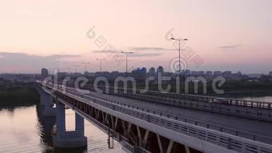 汽车在城市河流的桥上行驶。 无人机在日落背景下观看桥上的汽车交通。 城市建筑景观