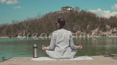 一个女人坐在湖边的<strong>木墩</strong>上，在阳光下冥想，在大自然中放松。 女孩回到框架里。