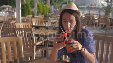 女孩拿着水果鸡尾酒坐在海滩附近的热带咖啡馆里。 沙滩暑假的概念..