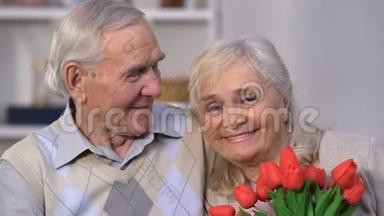 微笑的老年夫妇拥抱，女人闻花香，庆祝结婚纪念日