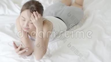 美丽的肖像年轻的亚洲女人微笑躺着看智能手机阅读社交网络与享受床上