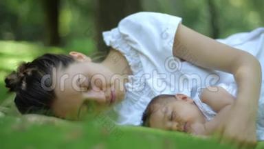妈妈吻她的孩子睡在户外的绿草上。 绿色夏日公园里快乐的幼儿妈妈.. 美丽美丽