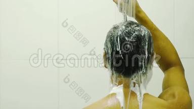 亚洲男人的背部用洗发水清洁头发，用手中淋浴的水清洗浴室