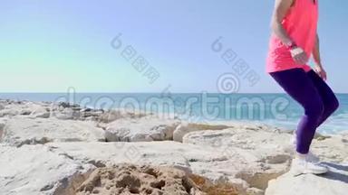 年轻迷人的白种人女孩跑过海边的岩石。 海浪冲击岩石海滩，水花飞溅