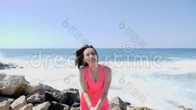年轻美丽的快乐女孩<strong>拍手</strong>，跳在一个岩石海滩上，海浪和水溅。 风和日丽的日子