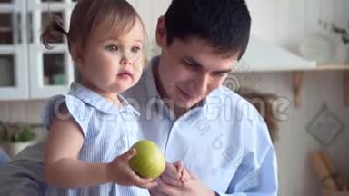 爸爸和女儿在厨房里，爸爸抱着女儿，女儿把一个绿色的苹果扔在地板上。