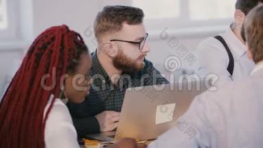 年轻认真专注的高加索软件开发人员，在现代笔记本电脑上工作，在多民族的团队会议上倾听。