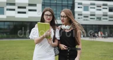 两个白种人漂亮的年轻女学生<strong>走路</strong>，一个女孩向另一个女孩展示一些书，她把它们带到了哪里