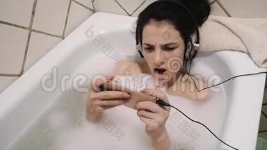 年轻女孩用防水智能手机耳机听音乐，在泡泡浴中唱歌