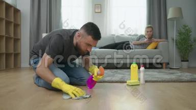 疲惫的丈夫打扫地板，妻子躺在沙发上用智能手机