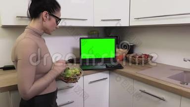女人在笔记本电脑旁边放着一碗沙拉，上面有绿色屏幕