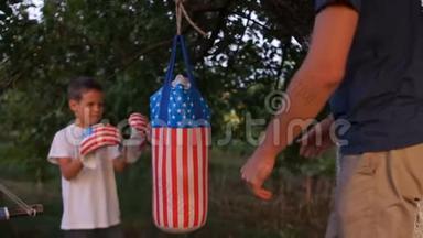 父亲教儿子拳击。 在房子附近的花园里用带有美国符号的梨进行户外训练。 父亲