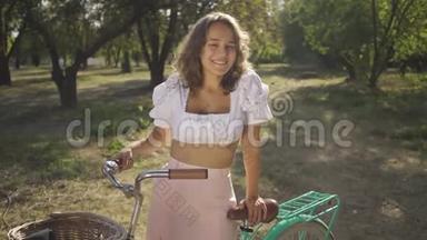 有魅力的年轻女人的肖像，卷发，骑着自行车站在花园或公园里。 <strong>农<strong>村</strong>生活。 复<strong>古</strong>