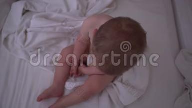 一个昏昏欲睡的小男孩坐在床上，慢慢地铺着白色的床上用品