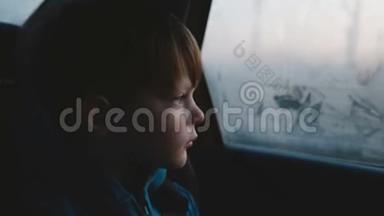 电影拍摄的小3-6岁可爱悲伤的白种人男孩在黑暗的傍晚乘车时从雾蒙蒙的车窗外看。