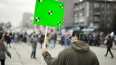 男人拿着绿色屏幕的<strong>海报</strong>，在城市集会上和人群一起走在街上，后景。