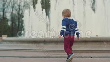一个小男孩在喷泉前散步。 与父母同行.. 父母照顾。 公园周末