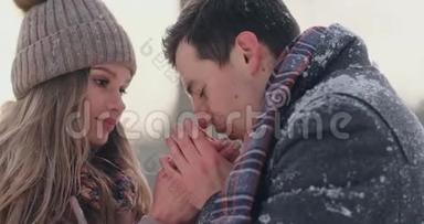 在一个白雪覆盖的公园里，一个有爱心的男人在冬天温暖`妻子的双手。