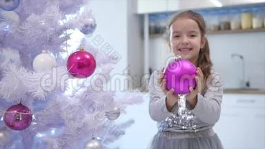 漂亮的小女孩<strong>正向</strong>相机伸出粉红色的宝布尔，站在圣诞树附近，微笑着。