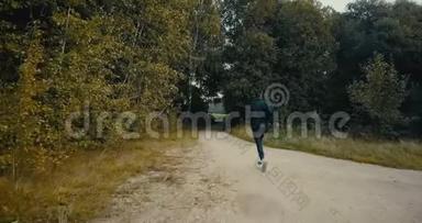 运动员跑到一个森林道路开口。 无人机后视图。 坚定的运动员在秋天穿越<strong>乡间小路</strong>。
