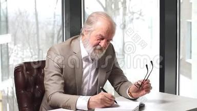 老教授，头发灰白，胡子留着漂亮的西装，在笔记本上记笔记。