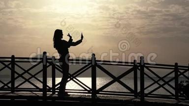 日出时，一个女孩站在桥上，在智能<strong>手机</strong>上<strong>制作</strong>自拍视频