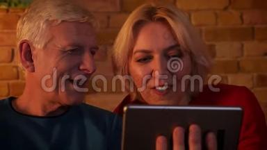 在平板电脑上播放视频的一对幸福的老夫妇的特写镜头笑着坐在室内的沙发上