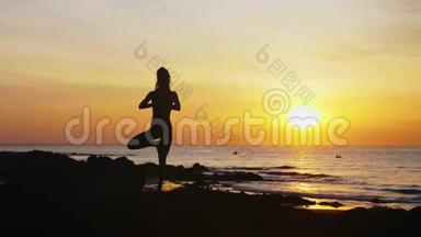 日落时分，在海边的沙滩上，一位手持双手的年轻女子摆姿势。