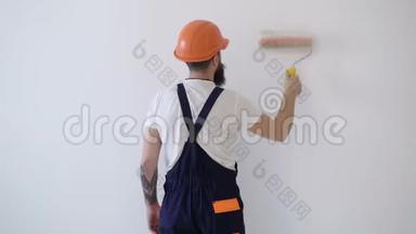 刷或滚涂白色油漆.. 家diy改造流程.. 油漆工的后视图用油漆辊涂墙壁