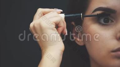 女人用化妆刷在睫毛上涂上黑色睫毛膏。 年轻漂亮的女人用睫毛膏涂眼睛