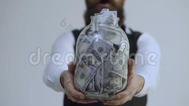 留胡子的人拿着一个装满钱的罐子，孤立在白色的背景上。 变得富有。 聪明地储存大钱。 节余