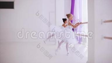 两个穿着白色芭蕾舞裙的儿童芭蕾舞演员正在芭蕾舞班的巴雷附近热身。