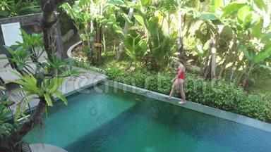 带热带花园的别墅无限游泳池鸟瞰图。女人走在池边欣赏丛林风光