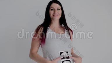 穿灰色衬衫的孕妇摆姿势。 母亲的肖像与婴儿的扫描。