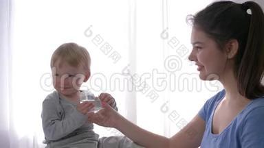 婴儿护理，哭泣的小男孩喝纯矿泉水从小<strong>妈妈怀里</strong>的玻璃到止渴近距离