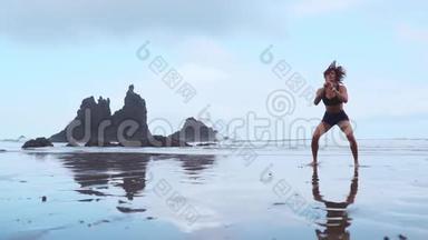女孩在海滩上蹲着训练后跳了出来，在大西洋附近有黑色的沙子。