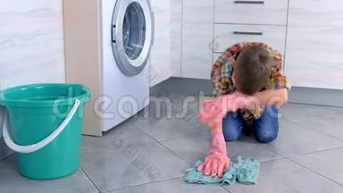 穿着橡胶<strong>手套</strong>的疲倦男孩在<strong>厨房</strong>里洗地板。 儿童`的家庭责任。
