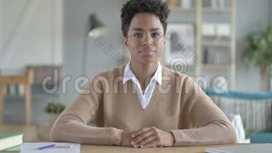 年轻的非洲女孩微笑着坐在工作桌旁