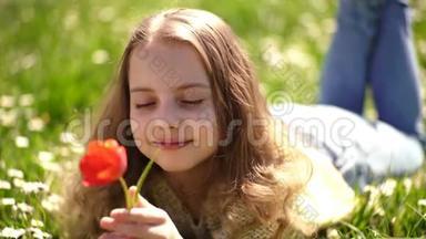 女孩躺在草地上，草地在背景上。 少女在<strong>梦</strong>幻的脸上捧着红色的郁金香花，享受香气.. 儿<strong>童</strong>享受