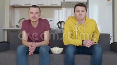 两个男人坐在沙发上用爆米花碗看电视上的<strong>足球赛</strong>