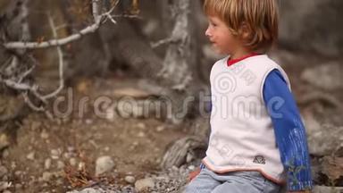 可爱的男孩在森林里玩。 一个小男孩从地上的石头上站起来，跑到一把旧塑料椅子上，爬上去