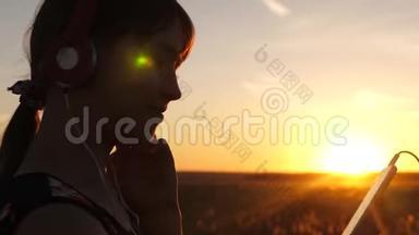 女孩旅行者在智能手机上听音乐，在美丽的春天日落的光<strong>线下</strong>。 带耳机的年轻女孩