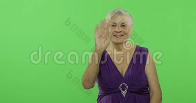 一位老年妇女向镜头挥手微笑。 老奶奶。 铬键