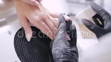 在美容院戴手套的女美甲师在涂胶前给顾客涂指甲油