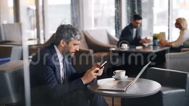 灰发商人在咖啡馆里用小玩意触摸智能<strong>手机屏</strong>幕