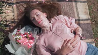 快乐可爱的女人躺在草坪上，床罩上美丽的花束旁，享受户外娱乐，顶景