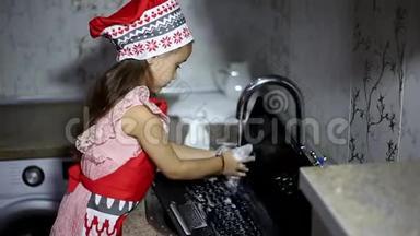 小女孩在厨房的水槽里洗手提电脑。 穿着红色围裙。
