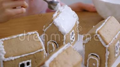 女人的手把姜饼屋的屋顶抹上糖霜。烹饪自制姜饼屋。
