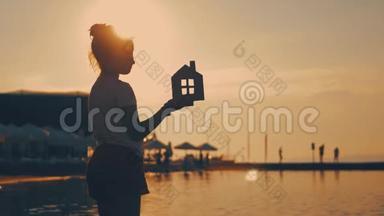 日落时，女孩在海滩上拿着纸房子。 人，梦想，<strong>家</strong>庭，房地产和<strong>家</strong>居理念.. 儿童梦