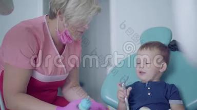 牙医戴着医用口罩和手套，准备检查坐在椅子上的无忧无虑的小男孩的牙齿。 淘气鬼